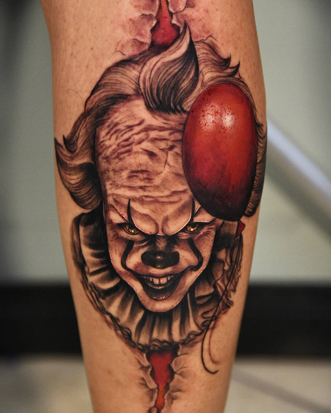 Detailed Pennywise tattoo on leg, featuring his menacing grin and a realistic red balloon